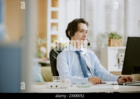 Young Caucasian call center male intern focused on work while using computer to write report Stock Photo