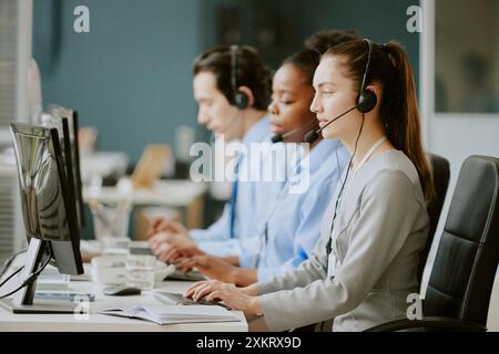 Young biracial call center operators sitting at work desk with electronic devices and office supplies on top in modern and cozy office Stock Photo