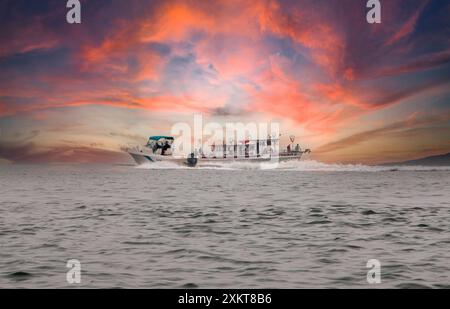 Fire Island, New York, USA - 9 July 2024: boat sails through calm waters as a mesmerizing, colorful sunset unfolds in the background. The vivid hues o Stock Photo