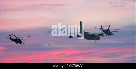 Jones Beach, New York, USA - 29 May 2022: A large military cargo plane is flying in formation with two helicopters, in a dramatic pink sky. Stock Photo
