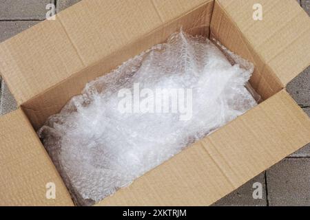An open cardboard box with bubble wrap inside of it lying on tiles. Close up. Stock Photo