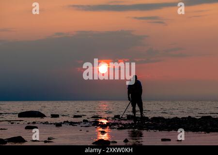 A photographer on a rocky beach lines up a shot as the sun sets over Lake Huron. Stock Photo