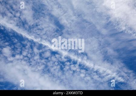 Old jet contrail through blue sky and white cirrus and cirrocumulus  clouds, Finland Stock Photo