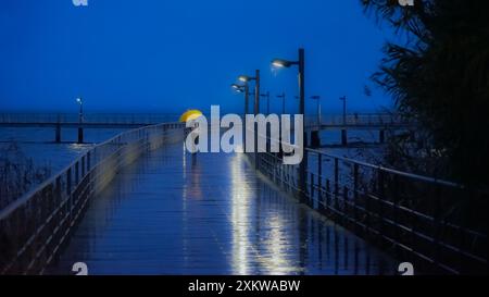 Pedestrian area with human figure with yellow umbrella on his back, on a rainy night with Vasco da Gama bridge located in Lisbon. Stock Photo