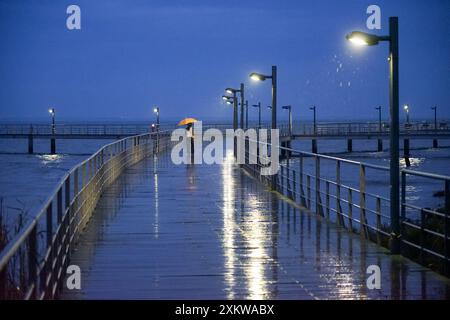 Pedestrian area with human figure with yellow umbrella on his back, on a rainy night with Vasco da Gama bridge located in Lisbon. Stock Photo