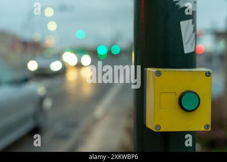 Green button with yellow frame to stop traffic on crosswalk with blurred car traffic background Stock Photo