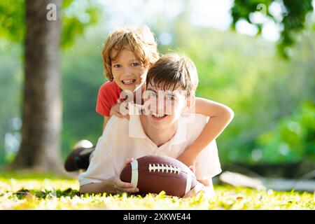 Family playing American football. Kids play rugby in sunny summer park. Father and children throw ball, run and laugh. Healthy outdoor sport activity. Stock Photo