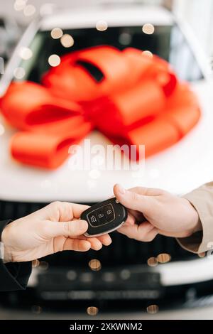 Vertical cropped shot of unrecognizable female seller giving car key and congratulating male after successful deal in auto dealership, Stock Photo