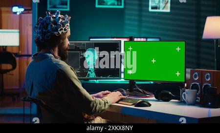 IT admin coding and using EEG headset to upload brain into mockup computer, gaining immortality. Neuroscientist engineering transhumanism experiment on isolated screen PC, camera A Stock Photo