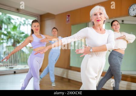 Active senior woman performing dance elements during lesson with female group in modern school for adults Stock Photo