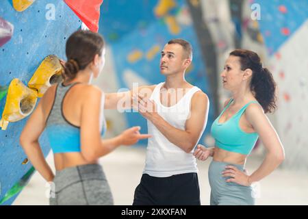 Athletic man and two sporty women discussing climbing options near climbing wall Stock Photo