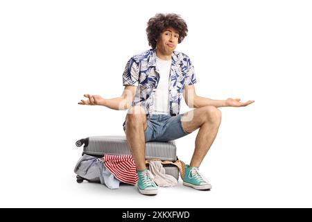 Young man sitting on top of a suitcase full of clothes isolated on white background Stock Photo