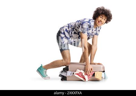 Young man trying to close suitcase full of clothes isolated on white background Stock Photo