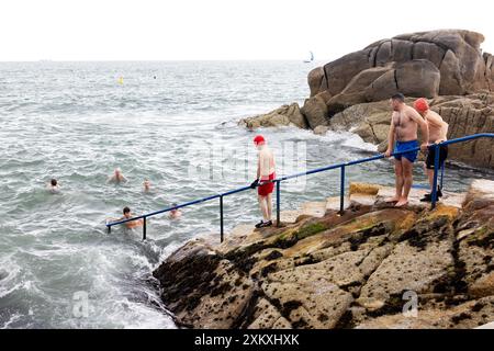 A group of men and women enter and swim in the cold water of the Irish Sea at The Forty Foot swimming hole in Sandycove, Dublin, Ireland. Stock Photo