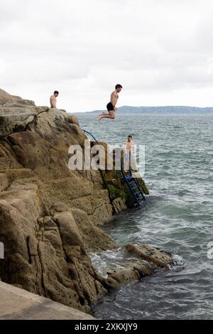 Swimmers jump off the rocks at Forty Foot, a famous swimming spot in Dublin Bay near Dun Laoghaire and Sandycove, Ireland. Stock Photo