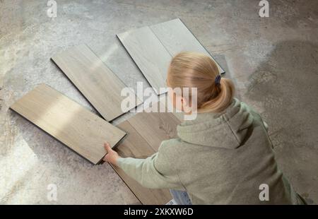 Woman Holds Luxury Vinyl Wood Samples On Concrete Floor In House. Choosing, Selecting Waterproof Flooring. Home Reconstruction. Vinyl Tiles Collection Stock Photo