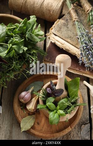 Different aromatic herbs, mortar with pestle, old books and spices on wooden table, flat lay Stock Photo