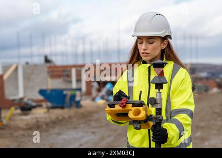 Female site engineer surveyor working with theodolite total station EDM equipment on a building construction site outdoors Stock Photo