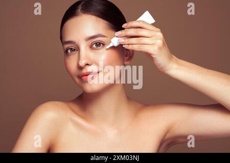 Beautiful woman using cream around the eyes. Video of woman with perfect makeup on beige background. Beauty and skin care concept Stock Photo