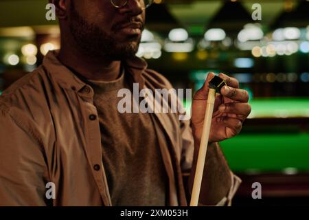 Hand of young African American male pool player rubbing tip of billiard cue with snooker chalk before game to prevent it from slipping Stock Photo