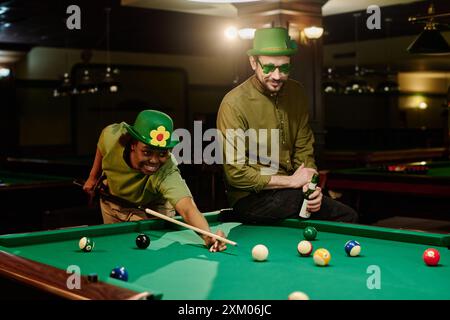 Happy young intercultural couple playing billiards while guy with bottle of beer sitting next to his girlfriend hitting pool ball with cue Stock Photo