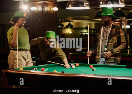 Group of happy young intercultural friends with billiard cues playing billiards by wide table and celebrating Saint Patrick day Stock Photo