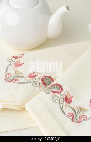 White Teapot and Floral Embroidered Napkins on a White Tablecloth Stock Photo