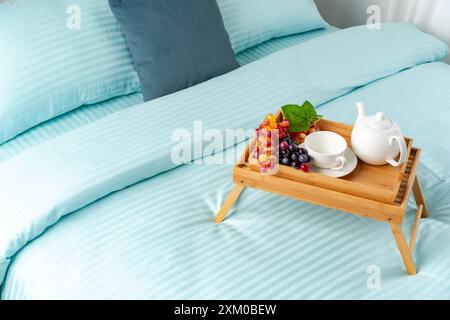 Wooden Breakfast Tray With Teapot, Grapes, and Cup on a Blue Bed Stock Photo