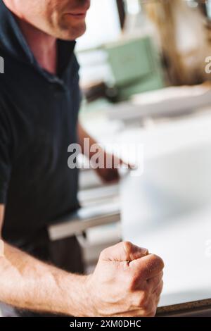 Carpenter is clenching his fist in a carpentry workshop, showcasing the physicality and strength required in this profession Stock Photo