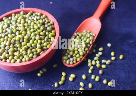 Green beans (Vigna radiata) in a wooden bowl and on a wooden spoon and some scattered in close view on black background. Stock Photo