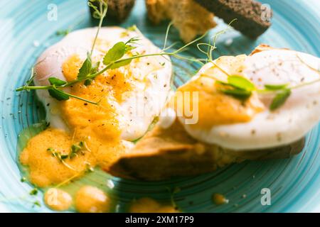 Eggs Benedict with Hollandaise sauce and toast on a turquoise plate on a white table. A place to copy a space. High quality photo Stock Photo
