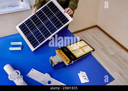 Green energy in street lighting, combining an LED lamp with built-in battery with solar panel, owner is busy installing purchased product. Stock Photo