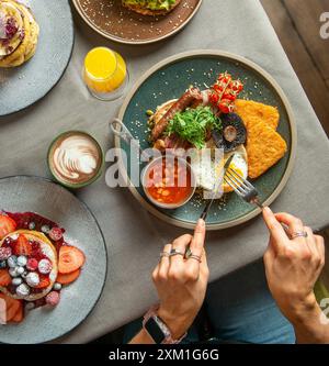English breakfast for breakfast or lunchtime on a plate with cutlery on a woman's hands. Stock Photo