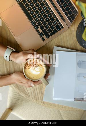 Woman's hands holding a cup of coffee on the wooden table. Stock Photo