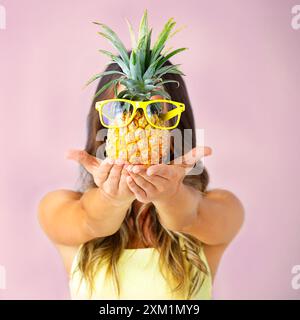 Hands, glasses and woman holding pineapple for cool fashion isolated on pink studio background. Cover, face and tropical fruit for healthy diet Stock Photo