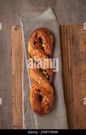 Braided handmade pastry with chocolate and custard, on parchment paper. Wooden background. Top view Stock Photo