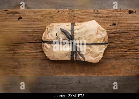 Cake wrapped in craft baking paper with black ribbon on a wooden table. Top view Stock Photo