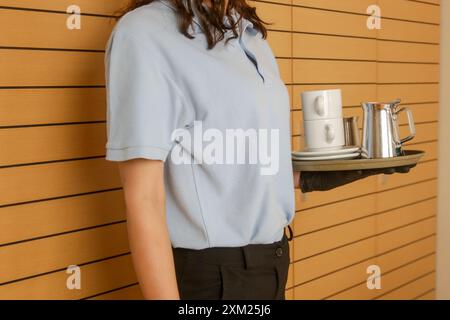 Room service hotel staff carries tray with hot beverages, coffee, tea and milk. Stock Photo