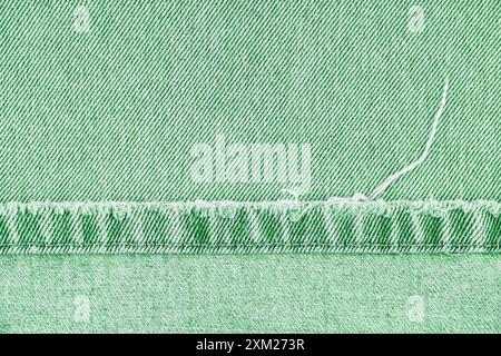 Green denim jeans pants shabby edge on jean fabric background, close up, macro. Ripped jeans stich, destroyed torn. Wallpaper, backdrop, design detail Stock Photo