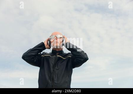 Attractive bald man with sunglasses and headphones. Outdoors with blue sky background Stock Photo