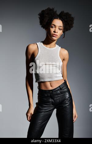 A stylish young African American woman poses in a white tank top against a grey backdrop. Stock Photo