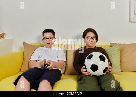 Two boys relax on a yellow couch watching TV. Stock Photo