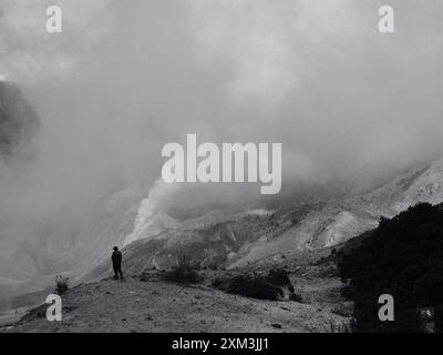 A person is standing on a hillside in the middle of a cloudy day. The sky is dark and the clouds are thick, creating a moody atmosphere Stock Photo