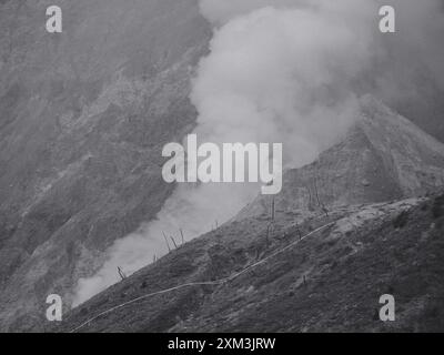 A mountain with a cloud of smoke rising from it. The smoke is dark and billowing, creating a sense of danger and destruction. The image evokes a feeli Stock Photo