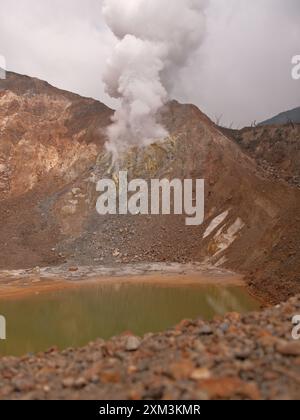 A large mountain with a large hole in the side and a large body of water. The water is green and the mountain is covered in rocks Stock Photo