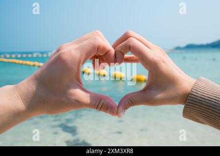 Couple two hands forming and making heart shape gesture on the beach. Concept of love and affection Stock Photo
