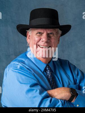 Older caucasian man wearing blue shirt and tie, and black hat with arms folded Stock Photo
