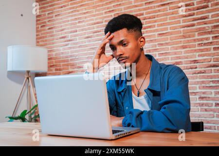 Exhausted and stressed African American man working on a laptop at home, suffering from a headache and mental fatigue. Adult male looks distressed and worried about her finances or job problem. High quality photo Stock Photo