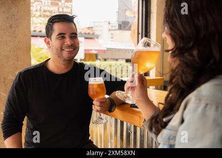 Smiling young man and woman enjoying a refreshing glass of beer at a daytime bar. The casual and lively atmosphere captures the joy of their social ou Stock Photo