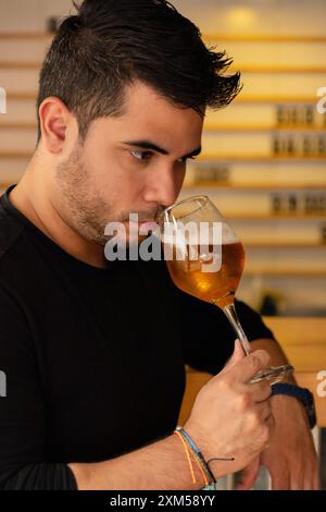A Latino man enjoys craft beer in a pub, concentrating on the aroma of the lager he is tasting. Stock Photo